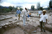 People at an archaeological site with low stone walls unearthed.