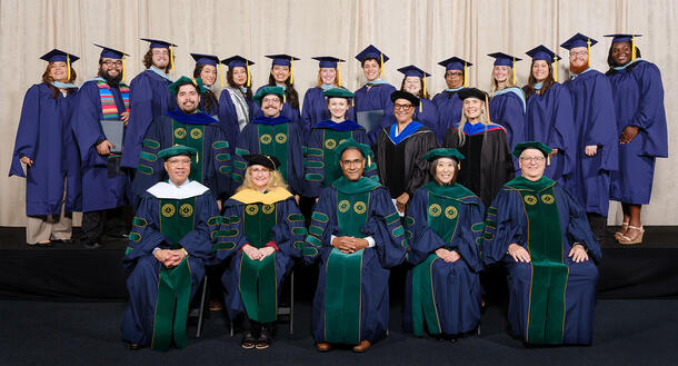 MAT graduates stand in the back row, Ph.D. graduates stand in the middle row, and honorary degree recipients are seated in the front row.