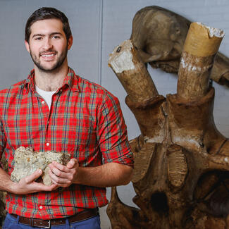 RGGS student Owen Goodchild stands next to a large fossil specimen and holds a smaller specimen in his hands.