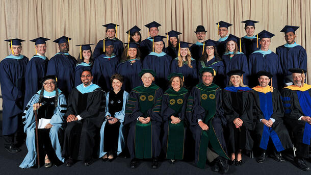 Two rows of MAT graduates wearing commencement robes stand behind a row of seated Museum mentors and teachers wearing ceremonial robes.
