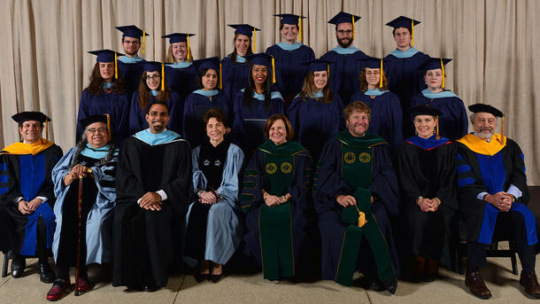 Two rows of MAT graduates wearing commencement robes stand behind a row of seated Museum mentors and teachers wearing ceremonial robes.