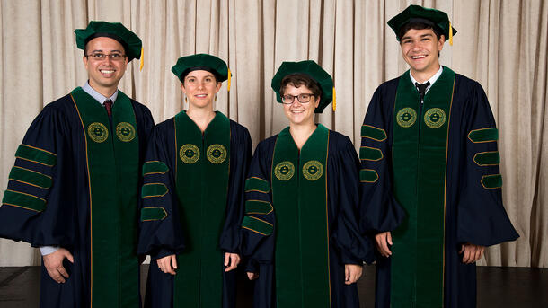 Four PHD graduates stand for a portrait wearing commencement robes.
