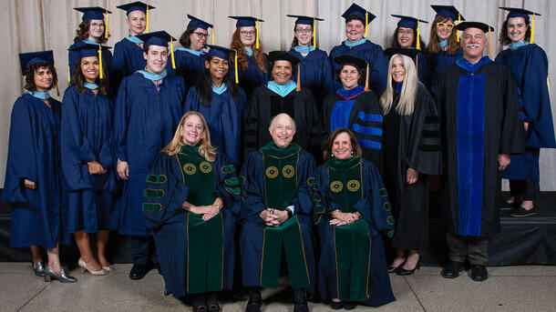 Two rows of MAT graduates wearing commencement robes stand behind a row of seated Museum mentors and teachers wearing ceremonial robes.
