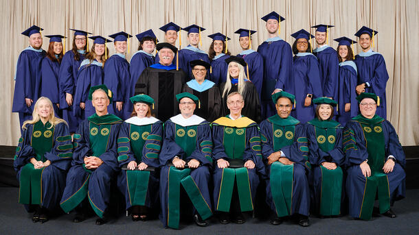 A row of MAT graduates wearing commencement robes stand behind a row of seated Museum mentors and teachers wearing ceremonial robes.