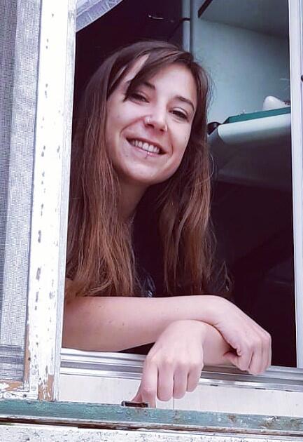 Sofia Paz Sedano leans on the wooden window frame of an open window.
