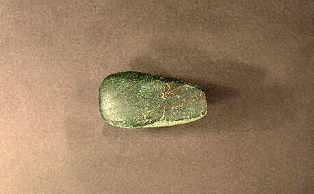 A piece of jadeite jade, dark green with lighter green spots, smoothed at the edges and likely used as an ax head between 250-500 AD, in Antigua.