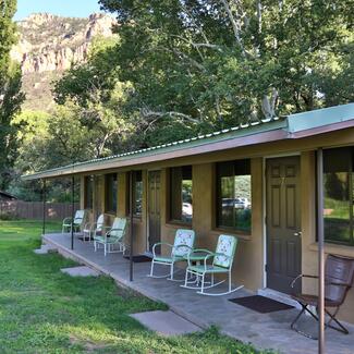 Front porch of lodging facility with metal chairs and trees and mountains in the background