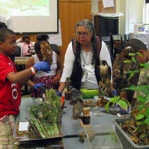 A woman working with children at a laboratory table with green plants.