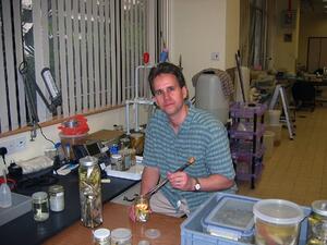 A man seated at a laboratory table, looking at the camera.