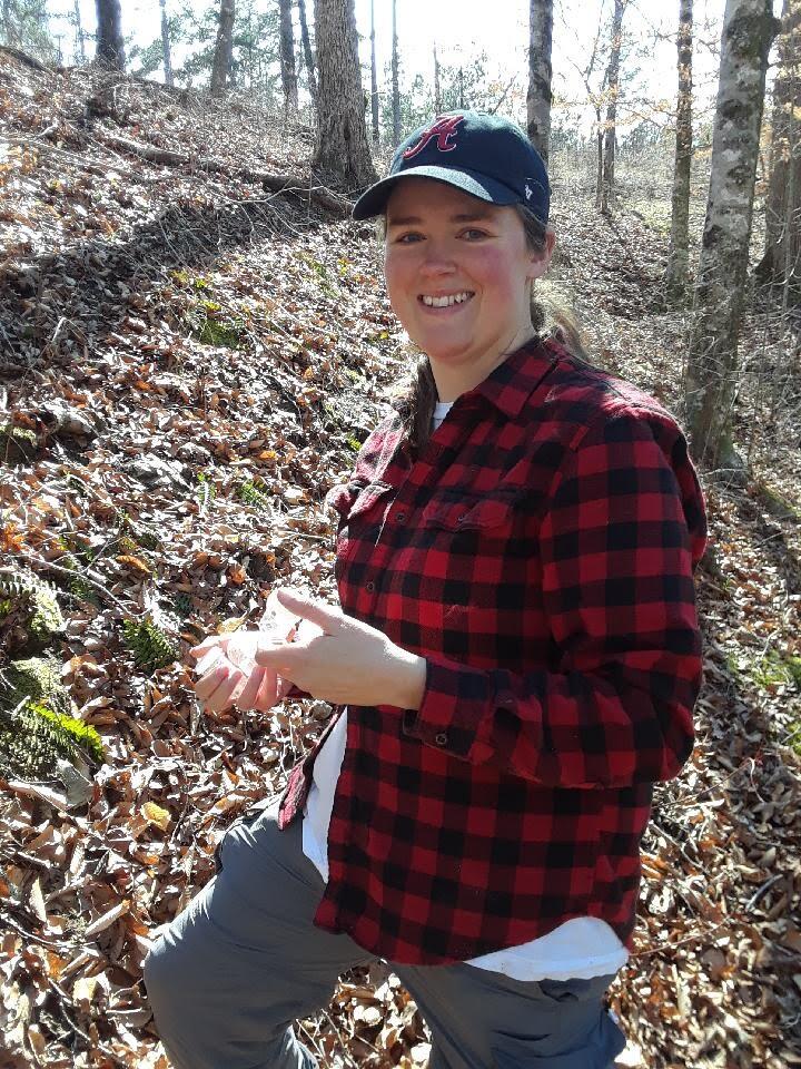 Lacie Newton stands in a forest, with fall leaves on the ground.