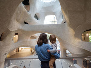 Adult stands and holds a child inside the Richard Gilder Center, looking towards the skylight and glass entrance-way.