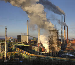 A factory with five smoke stacks with smoke emerging from them.