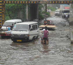 Five trucks, people on motorcycles, and people operating two carts in a flooded underpass area.