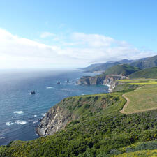 Coastline of lush cliffs beside bright water, with bright skies above.