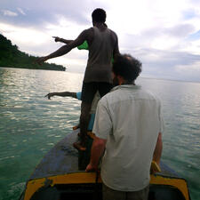 Five people on a boat, three of them standing, with coastline visible in background.