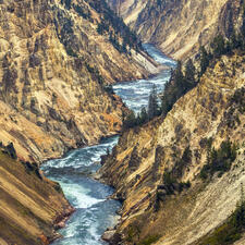 River running zig zag through a valley with steep mountains on each side and trees dotting the mountains.