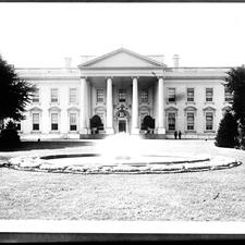 Historical photograph of The White House exterior with a fountain in front of the entrance.