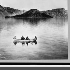 Historical photograph of a boat, filled with five people, on a lake surrounded by mountains.