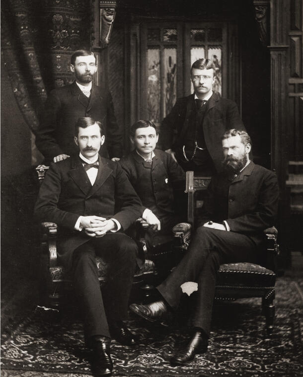 Five members of the New York State Assembly, three seated in the front and two standing with Theodore Roosevelt standing to the right.