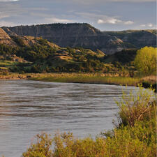 Body of water surrounded by grass, with rocky mountains in the background.