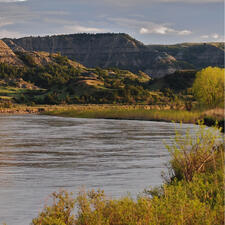 Body of water surrounded by grass, with rocky mountains in the background.