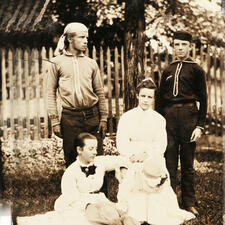 Theodore Roosevelt (standing, left), his wife Edith (seated, left), and two more family members pose outside.