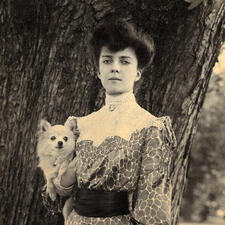 Alice Roosevelt, at age 18, standing in front of a tree and holding a puppy.
