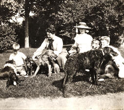 Four members of the Roosevelt family sit on the lawn and play with seven dogs.