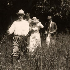 Theodore Roosevelt leads three of his children and other family members on a hike through tall grass.