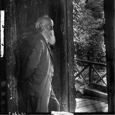 John Burroughs stands inside a wooden building, with a porch visible outside.