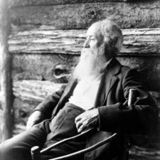 Writer John Burroughs sitting in a rocking chair in front of a wooden wall.