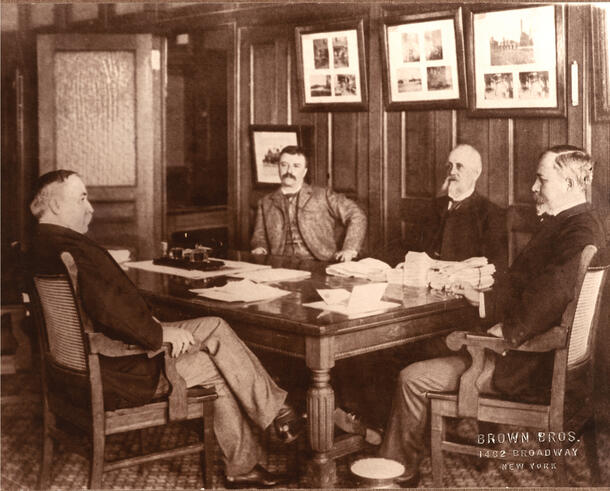 Theodore Roosevelt (third from right) sits at a table alongside three other people.