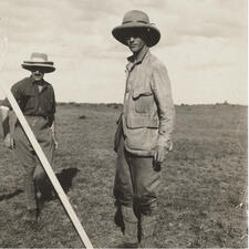 Two people stand in isolated landscape, both wearing wide-brimmed hats.