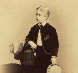 Young Theodore Roosevelt stands and leans one arm on a chair.