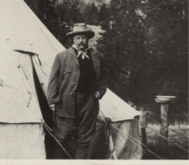 Theodore Roosevelt stands outside of a pitched tent, wearing a wide brimmed hat.
