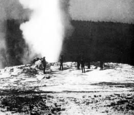 Historical photograph of people standing around an active geyser in Yellowstone.