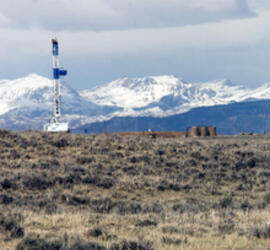 Grassy area with a crane and three cylindrical drums in the distance. There are snowy mountains in the farther background.