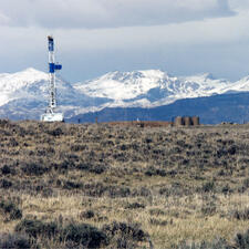 Grassy area with a crane and three cylindrical drums in the distance. There are snowy mountains in the farther background.