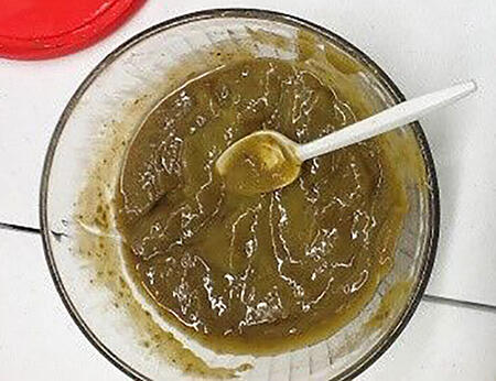 Glass bowl filled with a sticky looking substance (mango extract) with a plastic spoon resting inside.