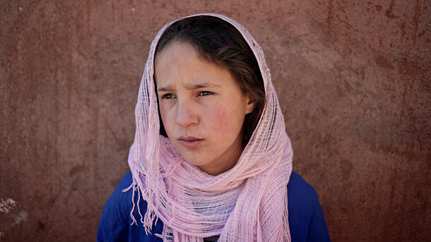 A young girl in a pink head scarf looks out.