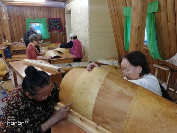 Two people attach pieces of curved bark to a structure. 