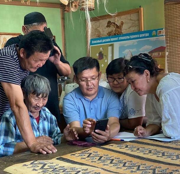 Six people gather around a table to view pieces of painted bark.