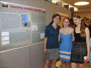 Three high school students stand near a poster display.